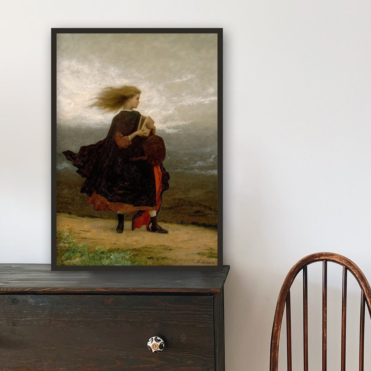 Framed fine art print of a young woman, on a wooden dresser, against a white wall.