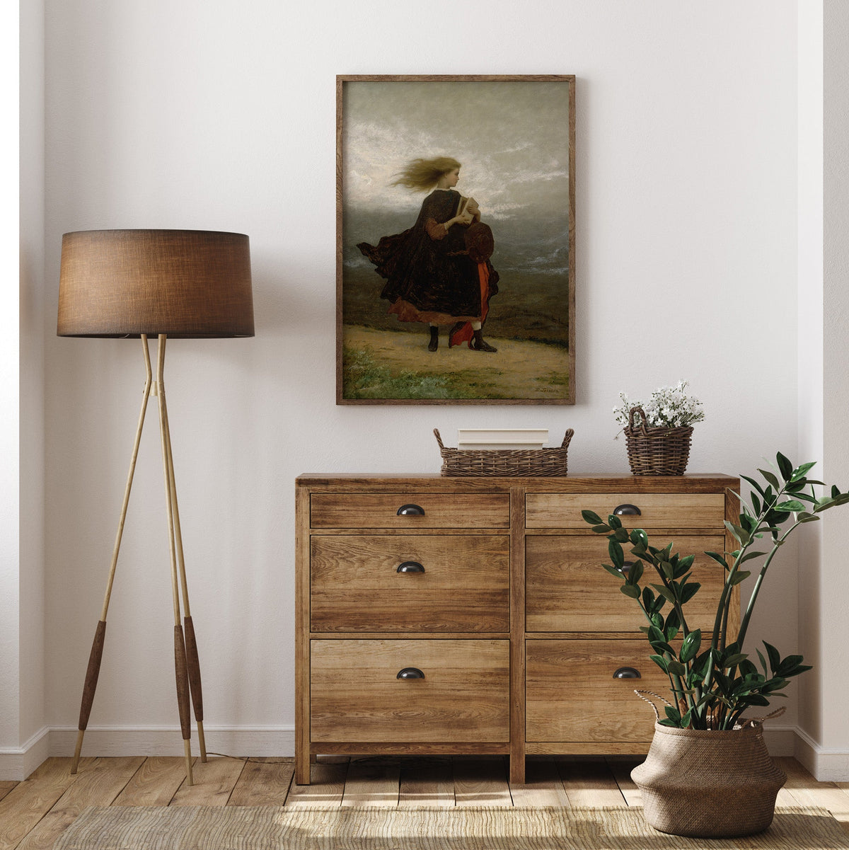 Wooden dresser with a lamp, plant, and portrait print, in a room.