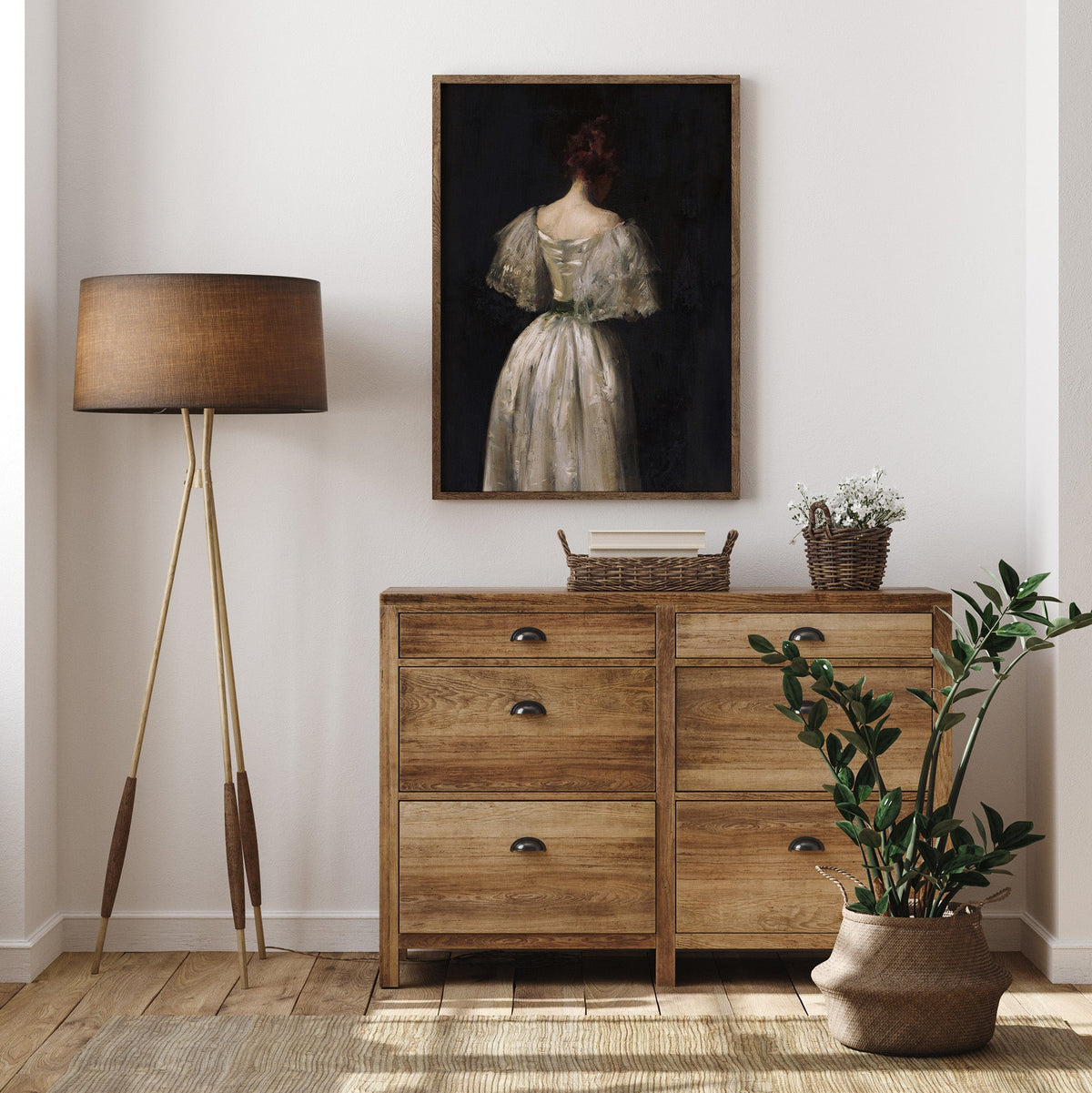 Wooden dresser with a lamp, plant, and framed female portrait print, in a room.