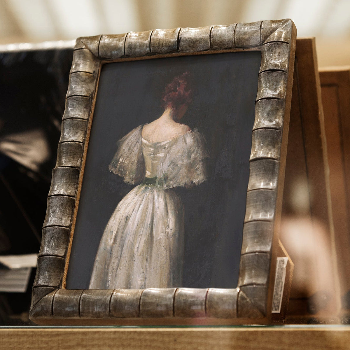 Small female portrait print in a white dress within a decorative frame on a wooden shelf.