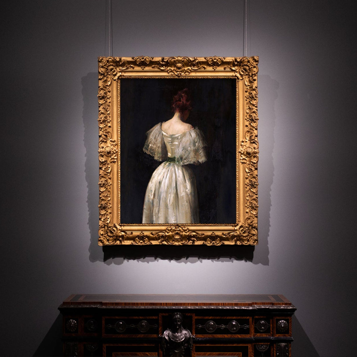 Framed print of a woman in a white dress on a gray wall in a gold ornate frame.