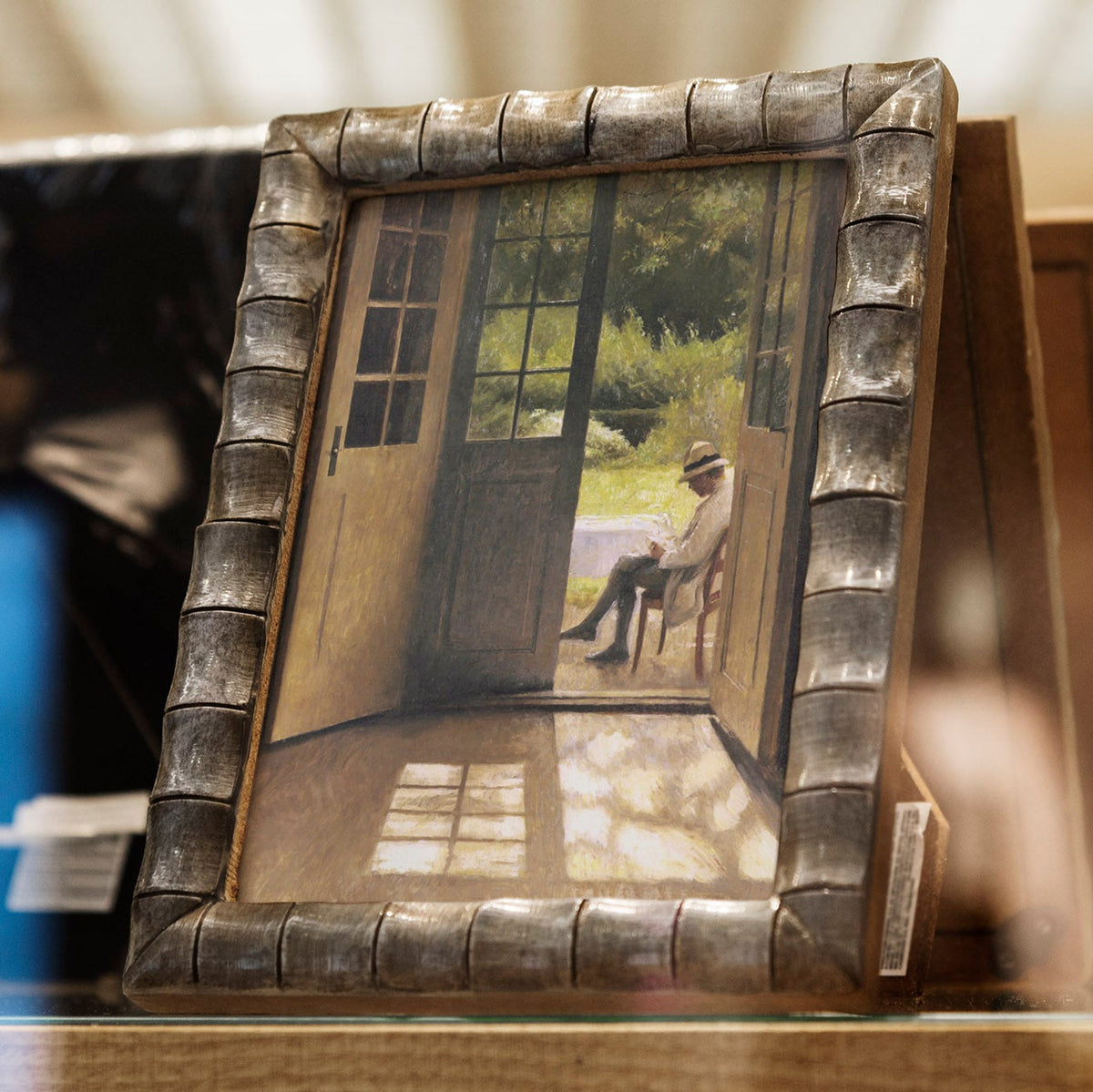 Framed picture of a man sitting in an open doorway, in a decorative frame on a table