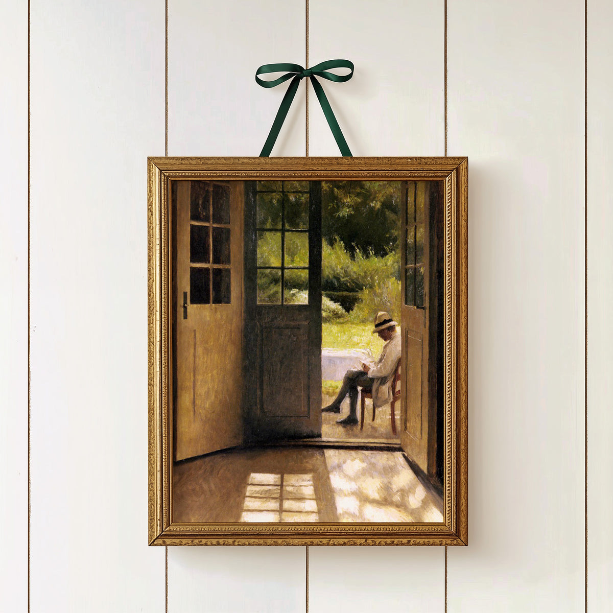 Framed artwork of a man sitting on a chair in a garden, hanging on a white wall.