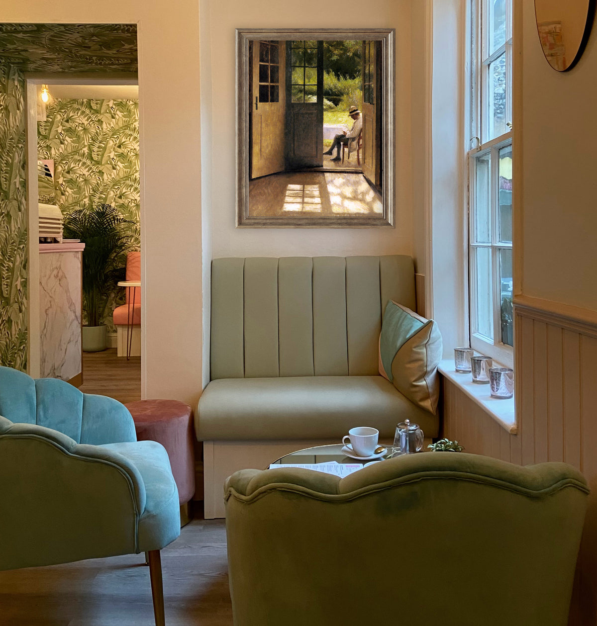 Cozy living room with a green sofa, armchair, and coffee table by a window and a framed portrait of a man sitting on a chair in an open doorway