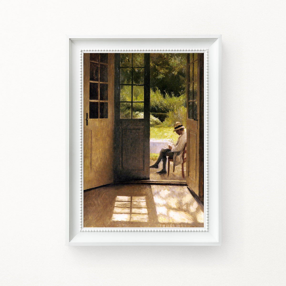 Framed artwork of a man sitting on a chair by a door, reading a book in a white frame hung on a white wall