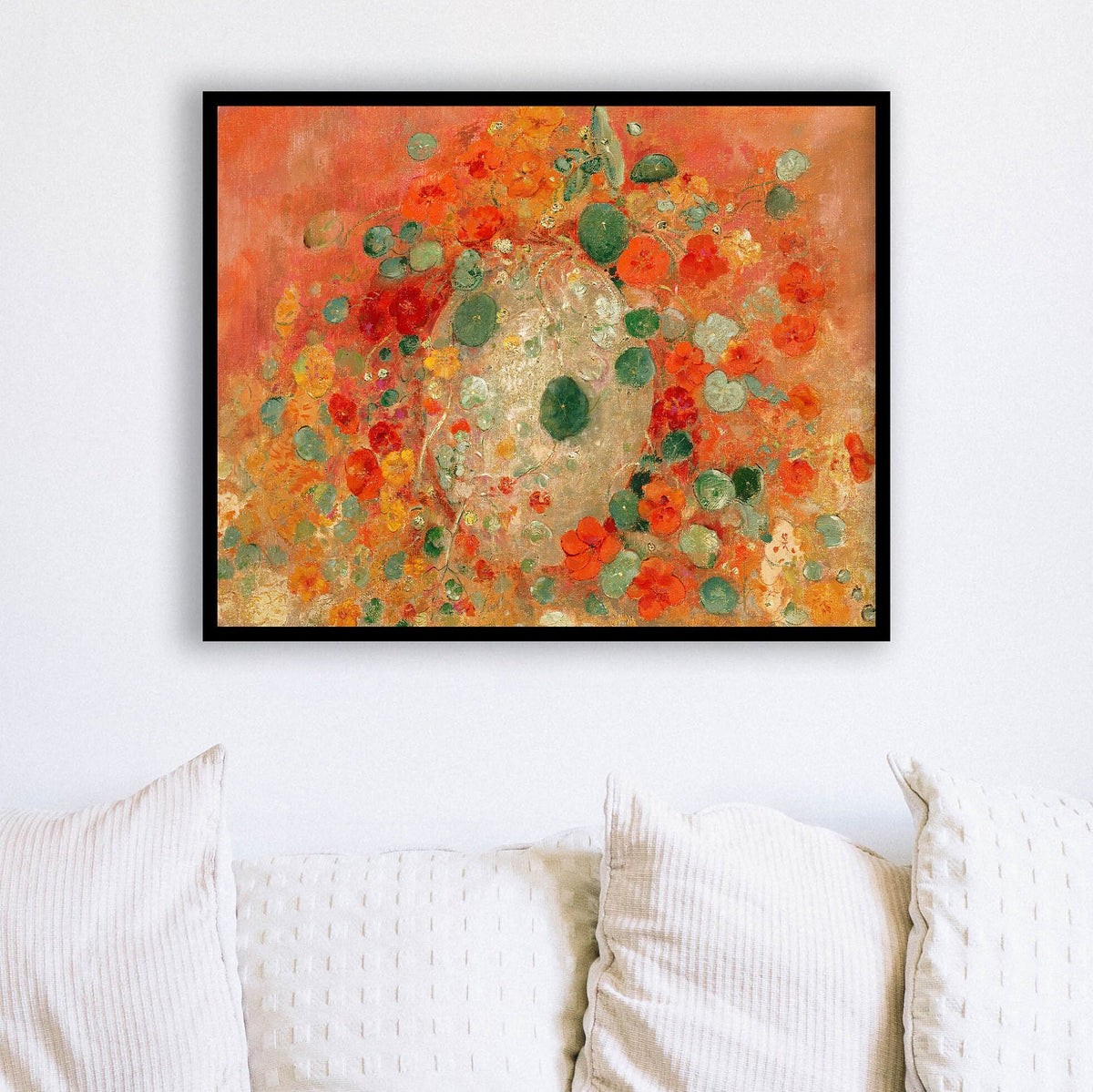 Framed abstract artwork with orange, red, and green colors on a white wall above a sofa.