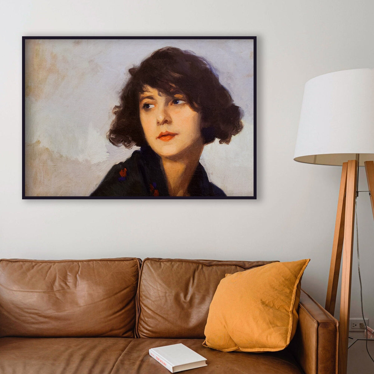 A fine art print of a portrait in oil of a young lady from the Art Deco period. The print is displayed in a thin black picture frame over a leather sofa.