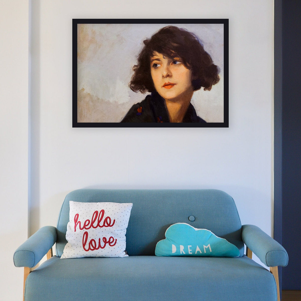 A fine art print of a portrait in oil of a young lady from the Art Deco period. The print is displayed in a black picture frame over a small blue sofa.