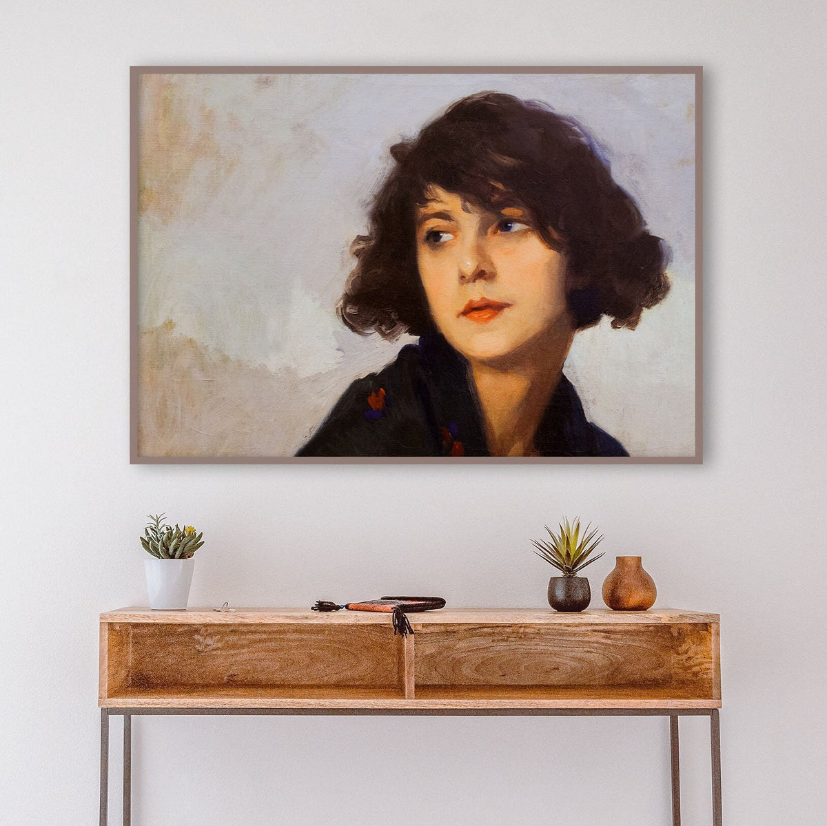 A fine art print of a portrait in oil of a young lady from the Art Deco period. The print is displayed in a thin wood picture frame over a console table.
