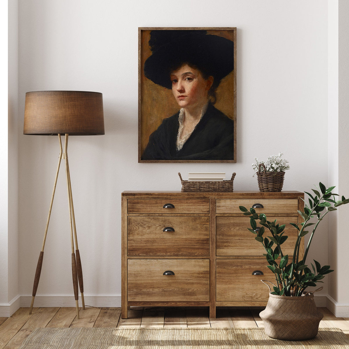 Wooden dresser with a lamp, plant, and portrait of a lady in a black hat, on a white wall.