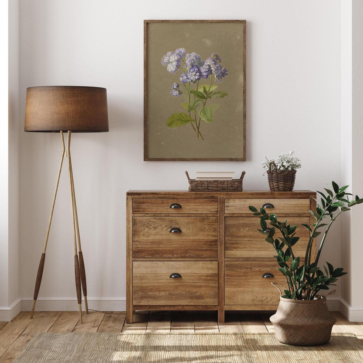 A fine art print of a delicate botanical illustration that features a sprig of purple heliotrope. The print is displayed hanging on the wall in a wooden picture frame, in a modern living room, above a wooden chest of drawers.