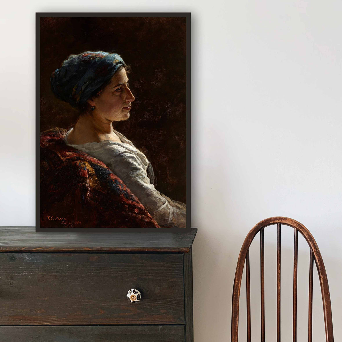 A wooden chair and dresser with a framed portrait above, in a room setting.