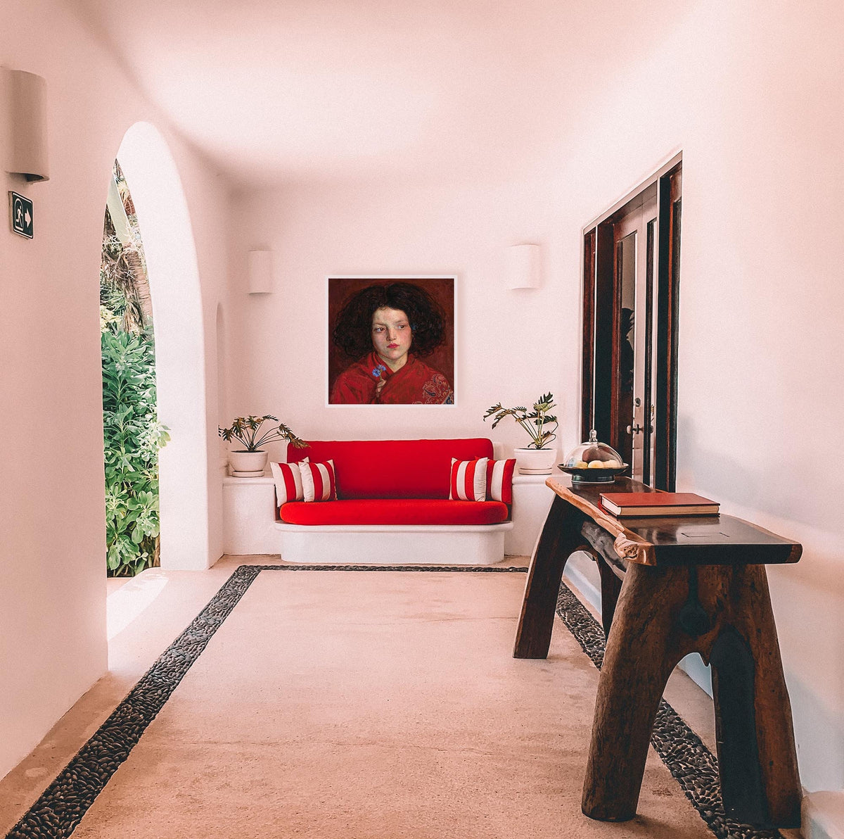 A fine art print of a beautiful oil painting of a young girl in a red shawl from mid 19th century. The print is displayed hanging on the wall in a luxury house above a bright red sofa.