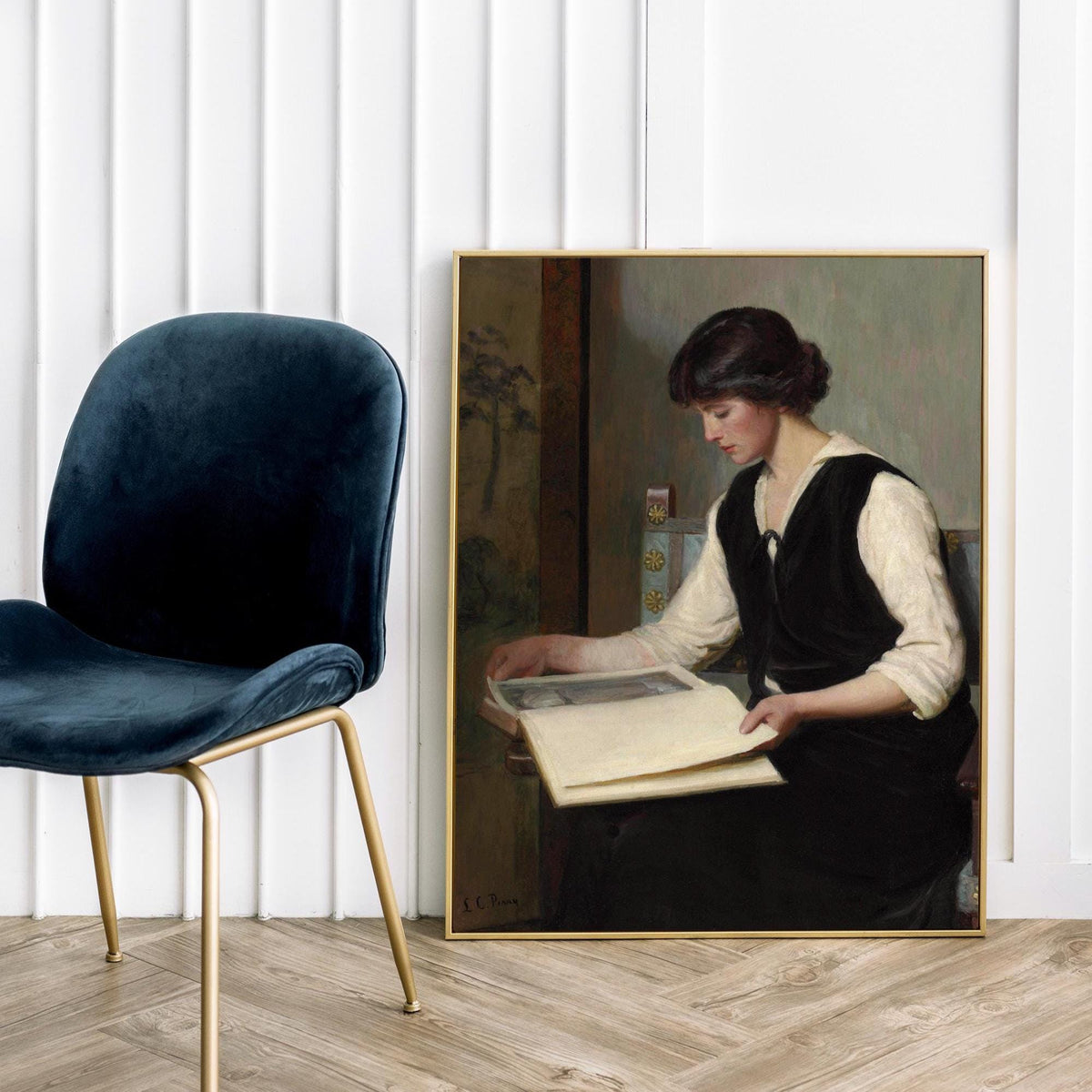 Framed print of a woman reading next to a blue chair on a wooden floor.