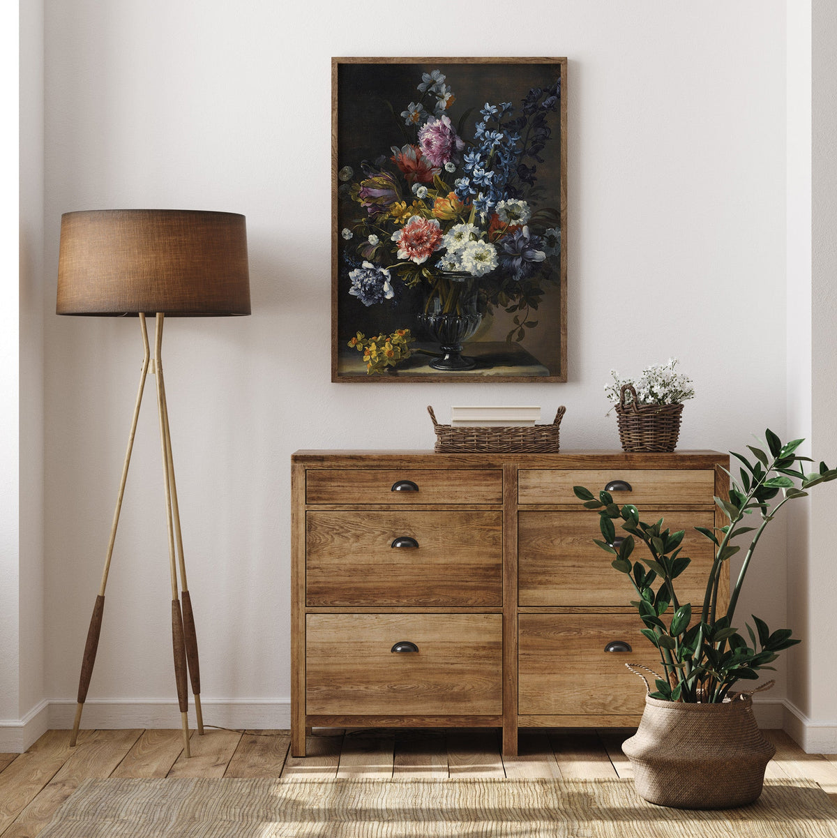 Framed floral print in a wooden frame above wooden drawers with a plant in front and next to a standard lamp.