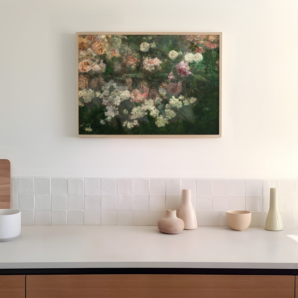 A framed art print of a rose garden in full bloom, hanging on a white wall in a kitchen above a counter top.