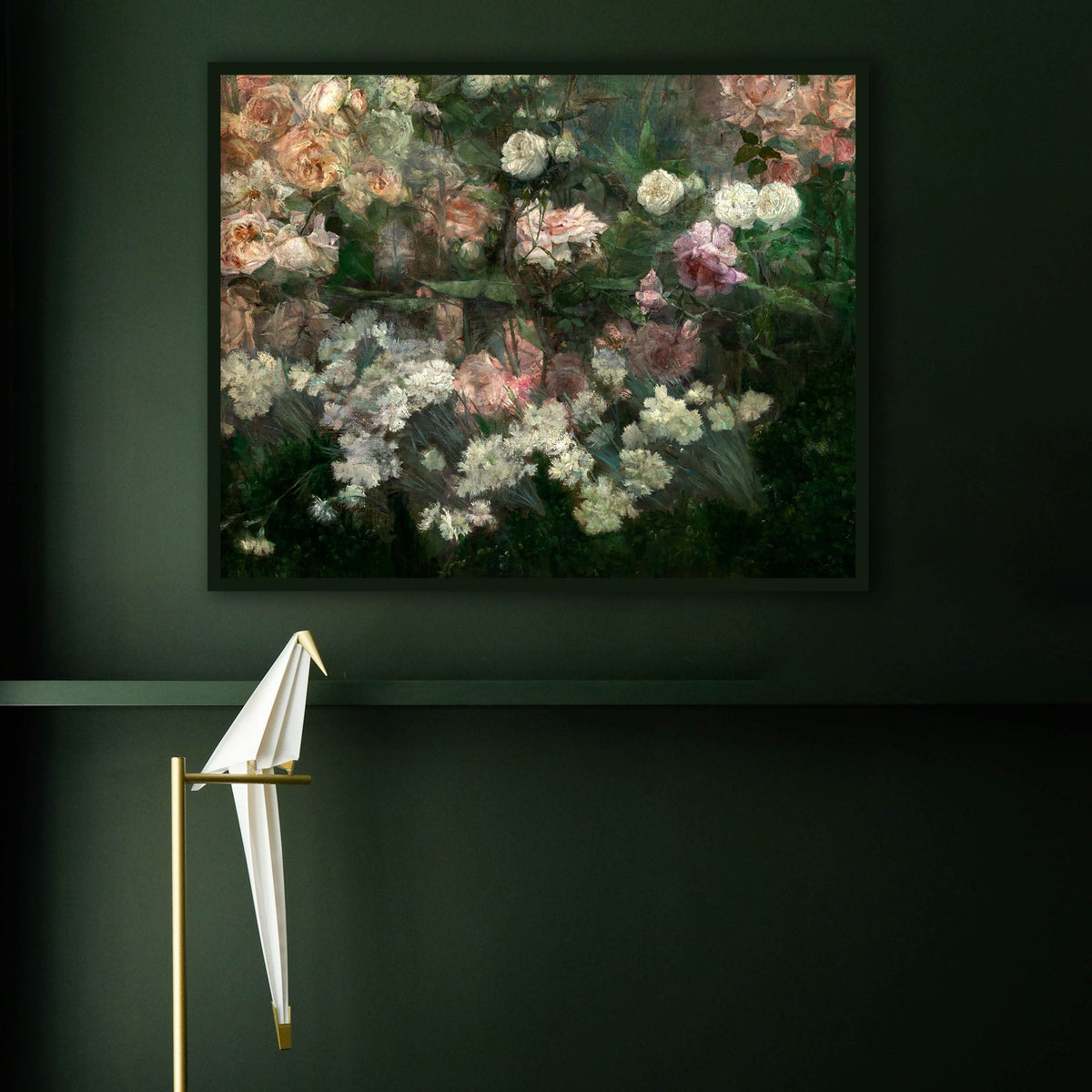 A framed art print of a rose garden in full bloom, hanging on a dark green wall with an origami bird resting on a perch in the foreground.