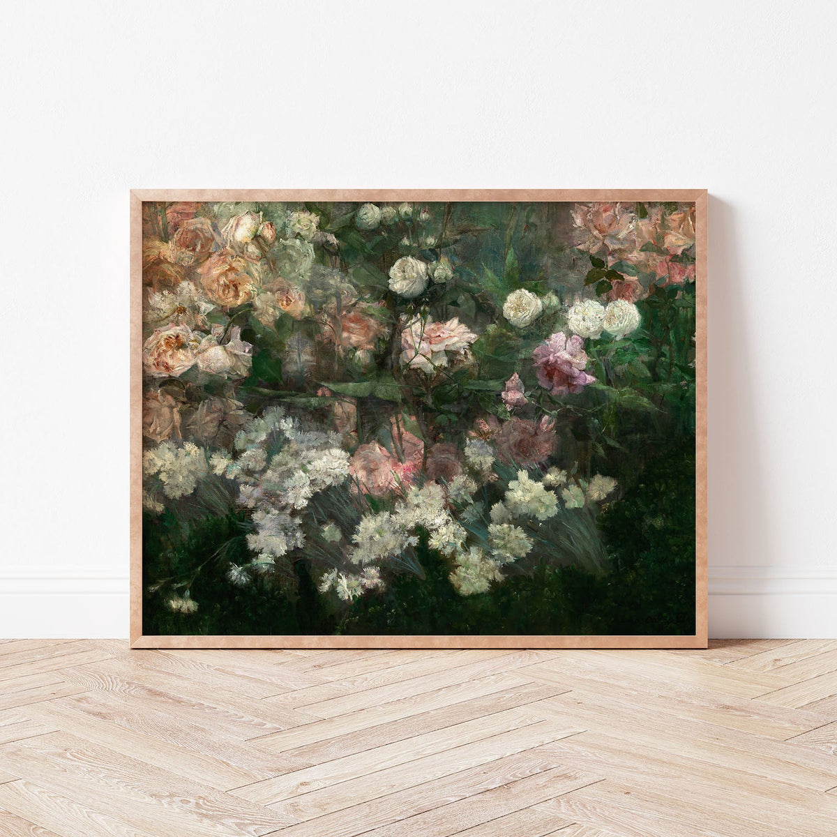 A framed art print of a rose garden in full bloom, resting against a white wall, on a wooden floor.