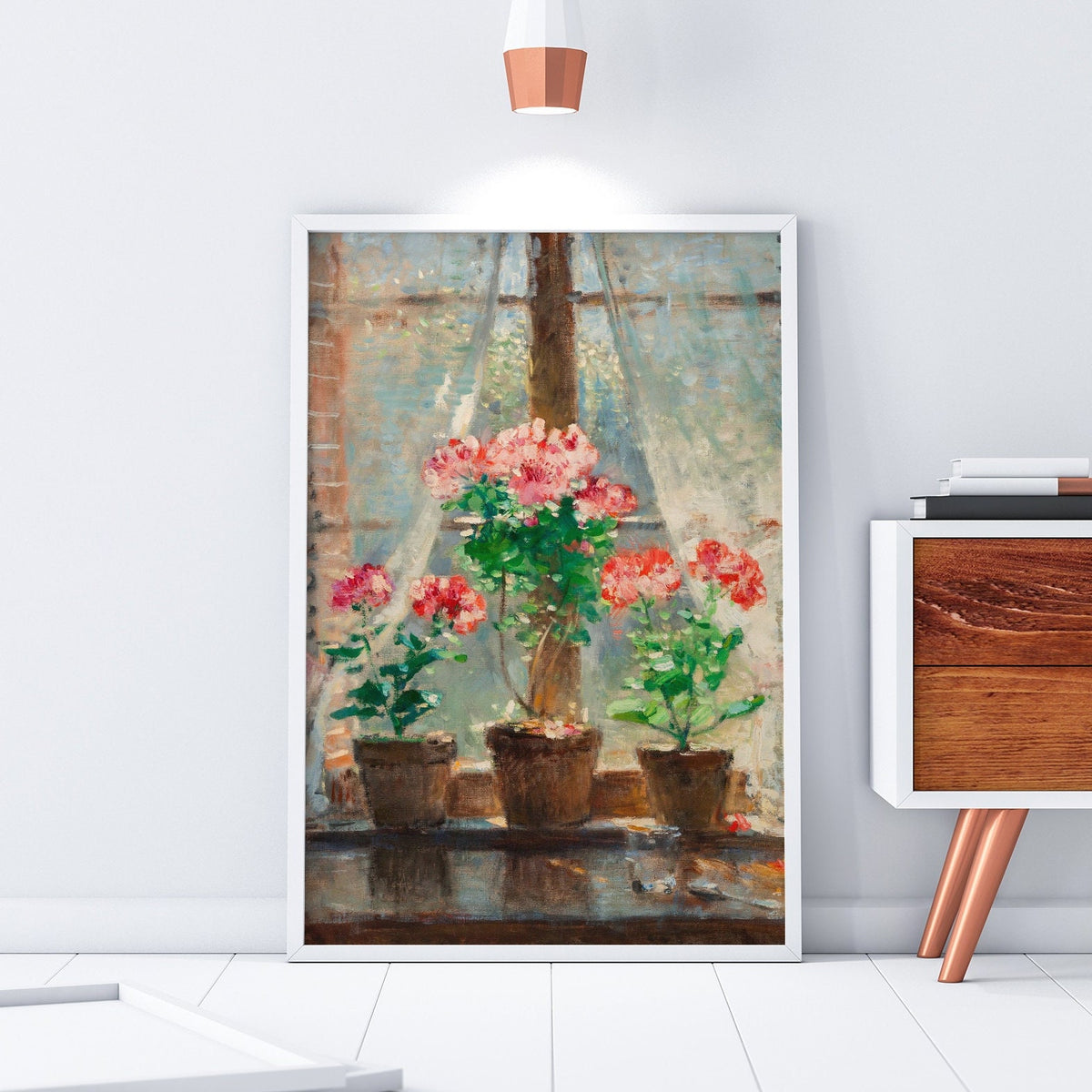 Framed print of potted flowers, resting on the floor in a white picture frame, in a room with modern decor