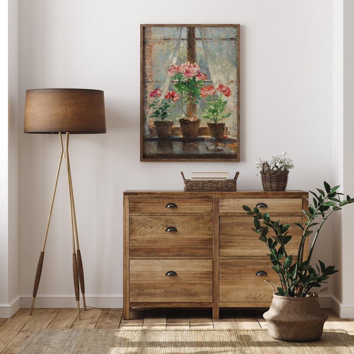 Wooden dresser with a lamp, plant, and framed print of red flowers, in a room.