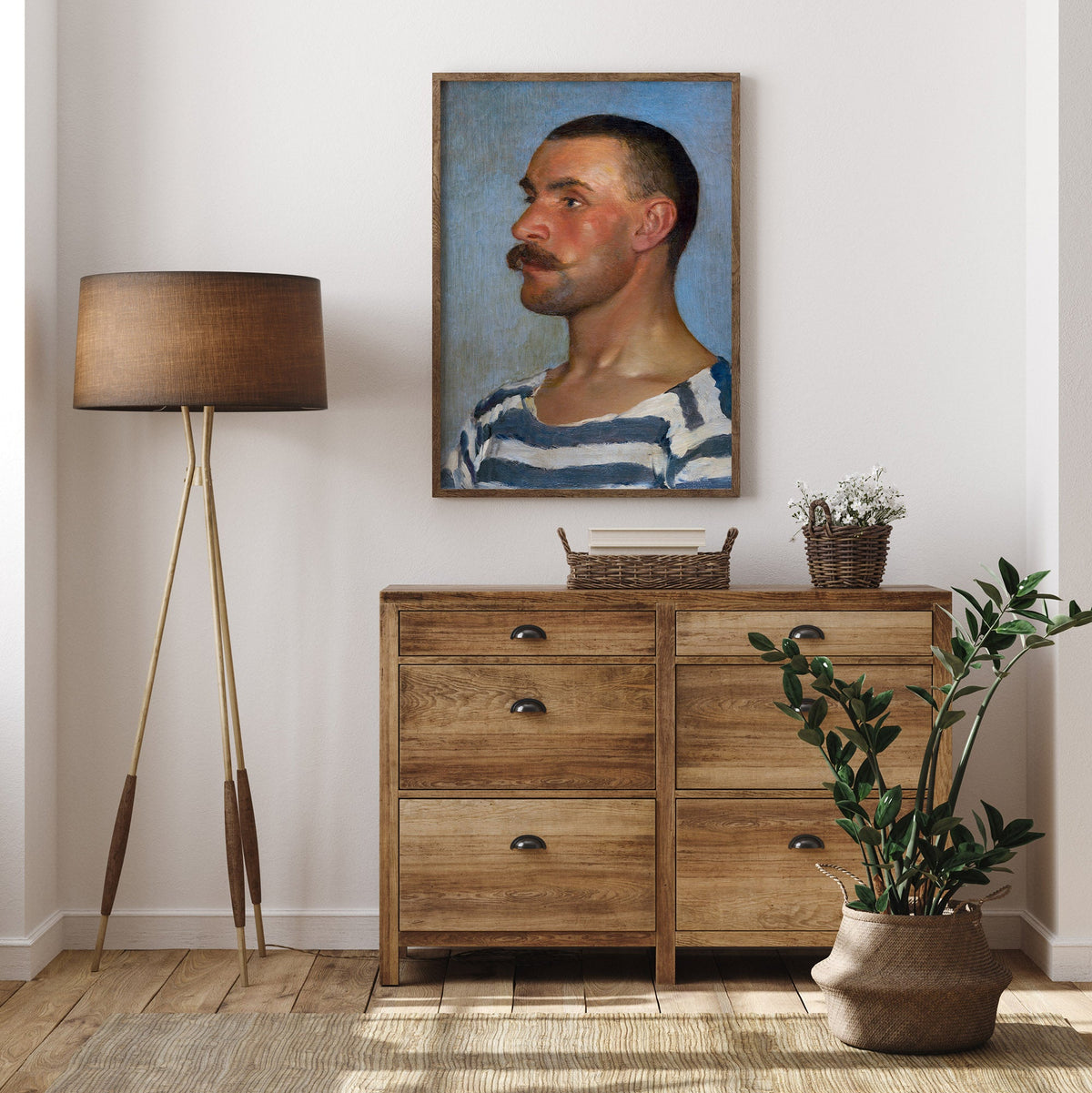 Room interior with wooden dresser, lamp, and plant against a white wall with a portrait of a man.