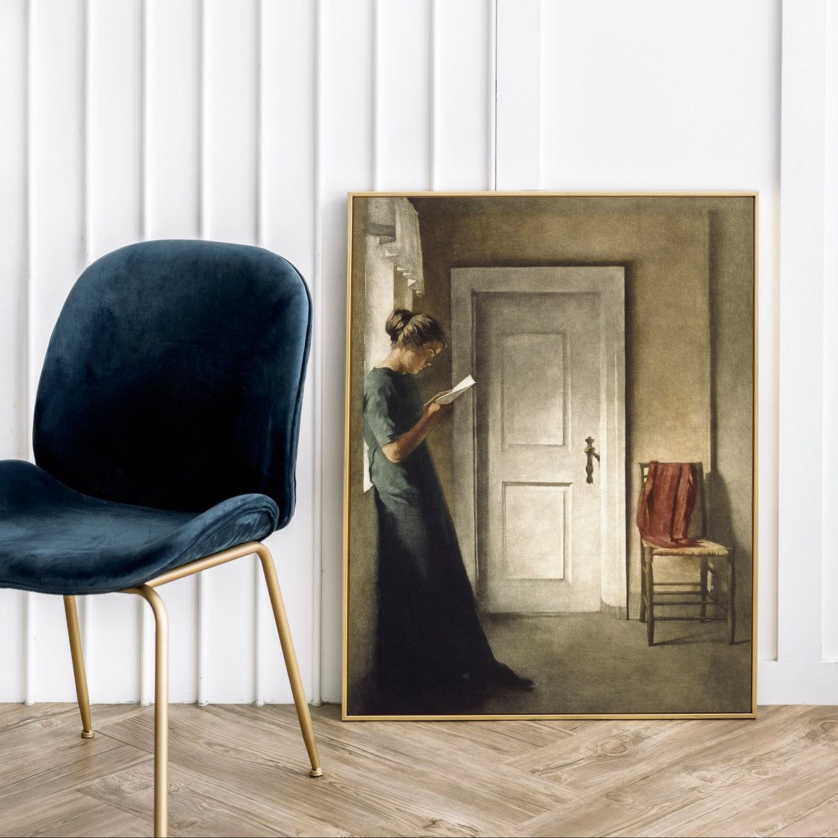 Framed painting of a woman in a room with a chair and lamp in the foreground.
