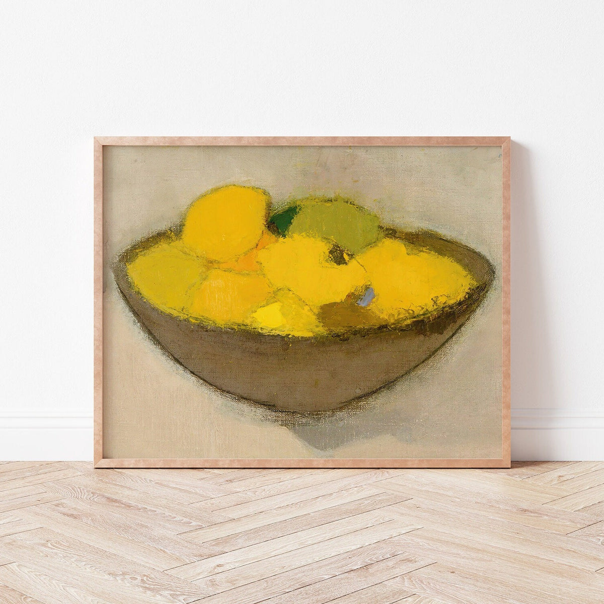 Framed print of a bowl of lemons on a neutral background, resting on a wooden floor.