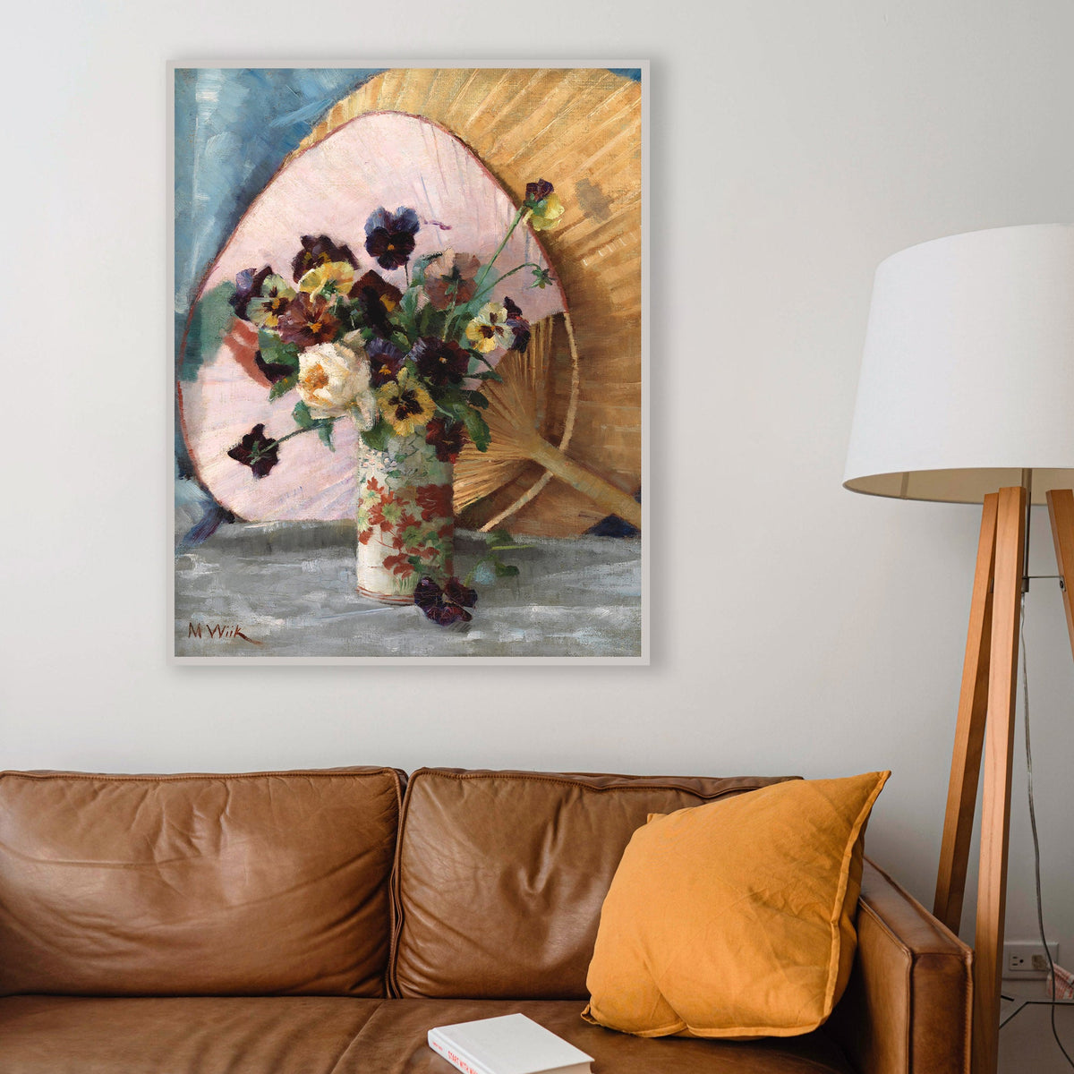Framed artwork of a floral arrangement with a fan above a brown leather sofa.