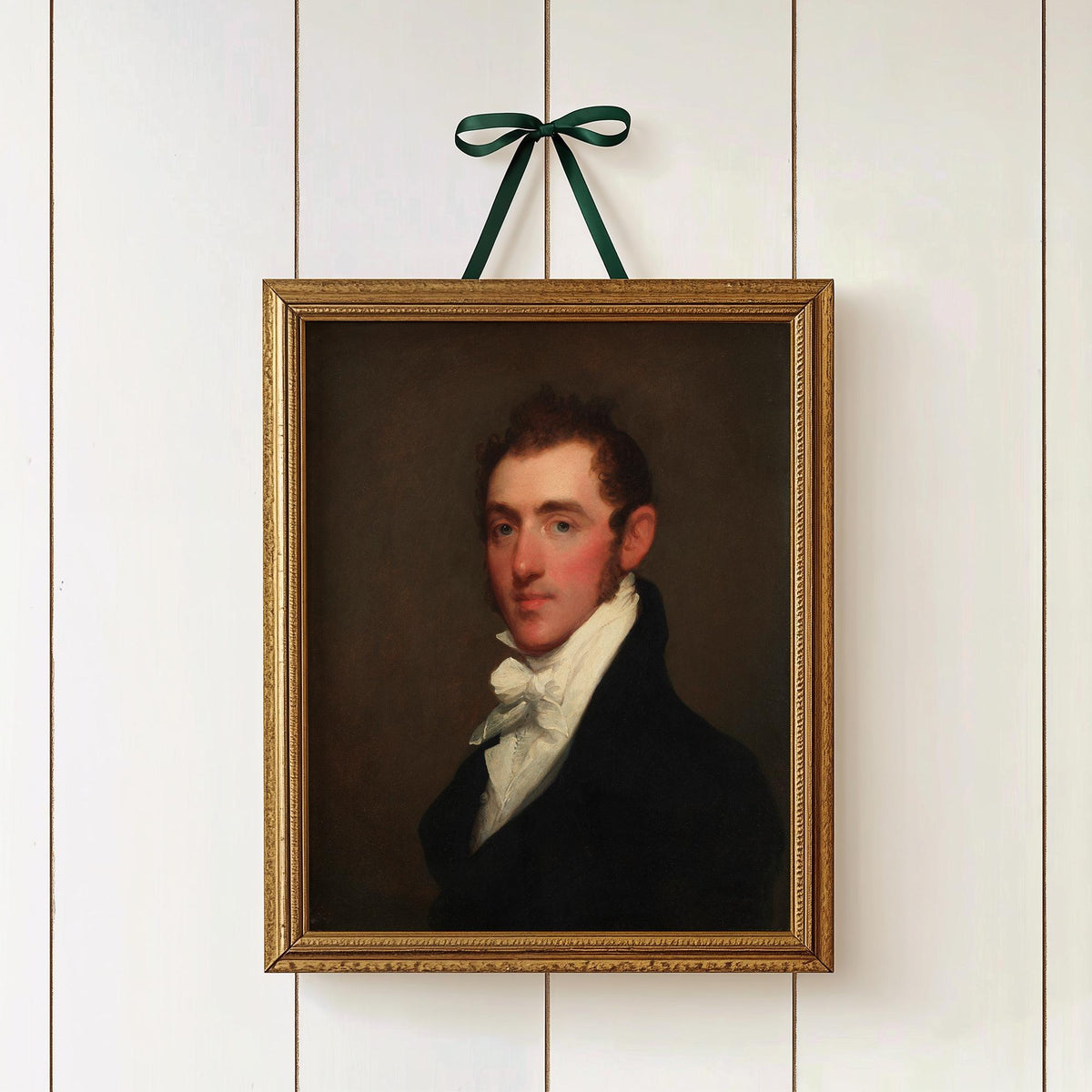 A fine art print of a Regency-era gentleman. The print is displayed hung on a white panelled wall in a gold picture frame, hung by a ribbon and bow.