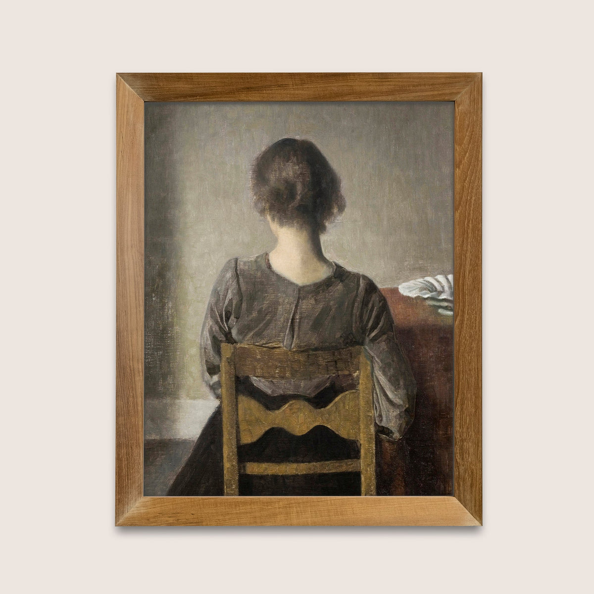 Framed painting of a woman sitting at a table with a wooden chair on a light gray background