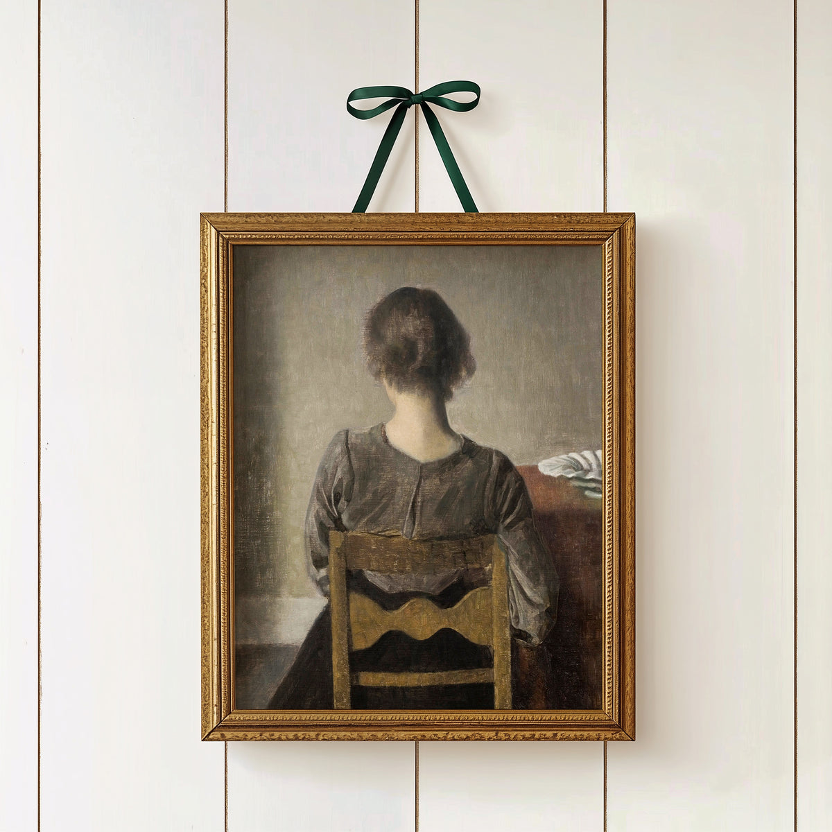 Framed portrait of a woman sitting on a chair against a white wall with a green ribbon.