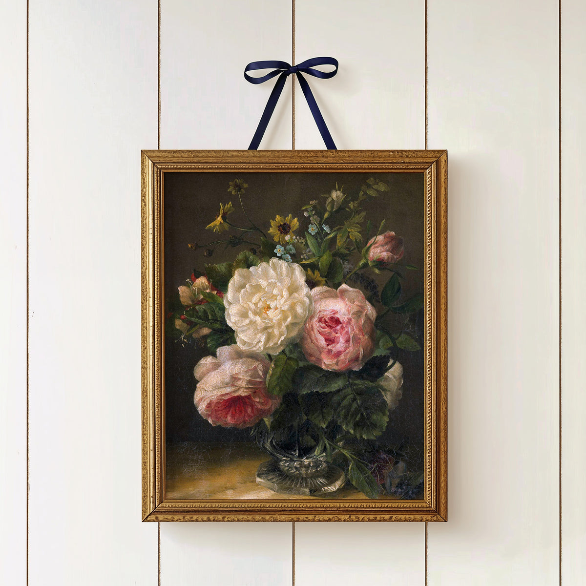 Gold-framed print of a floral bouquet on a white wall, hung by a blue ribbon