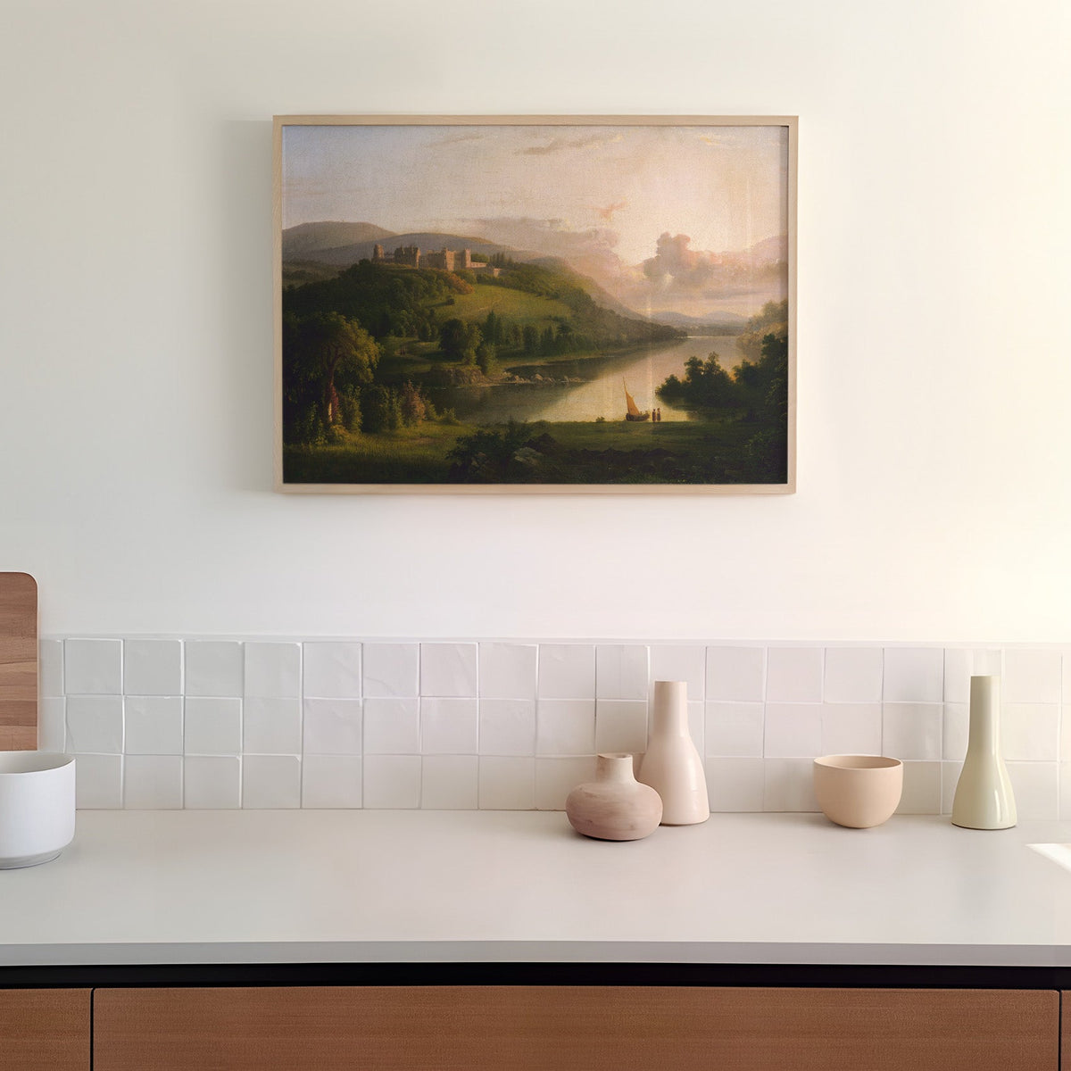 Framed landscape painting above a kitchen counter with decorative vases.
