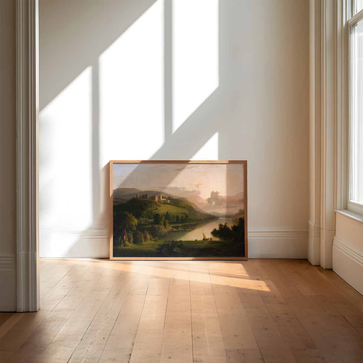 Framed landscape print resting against a wall in a bright room with sunlight streaming through windows.