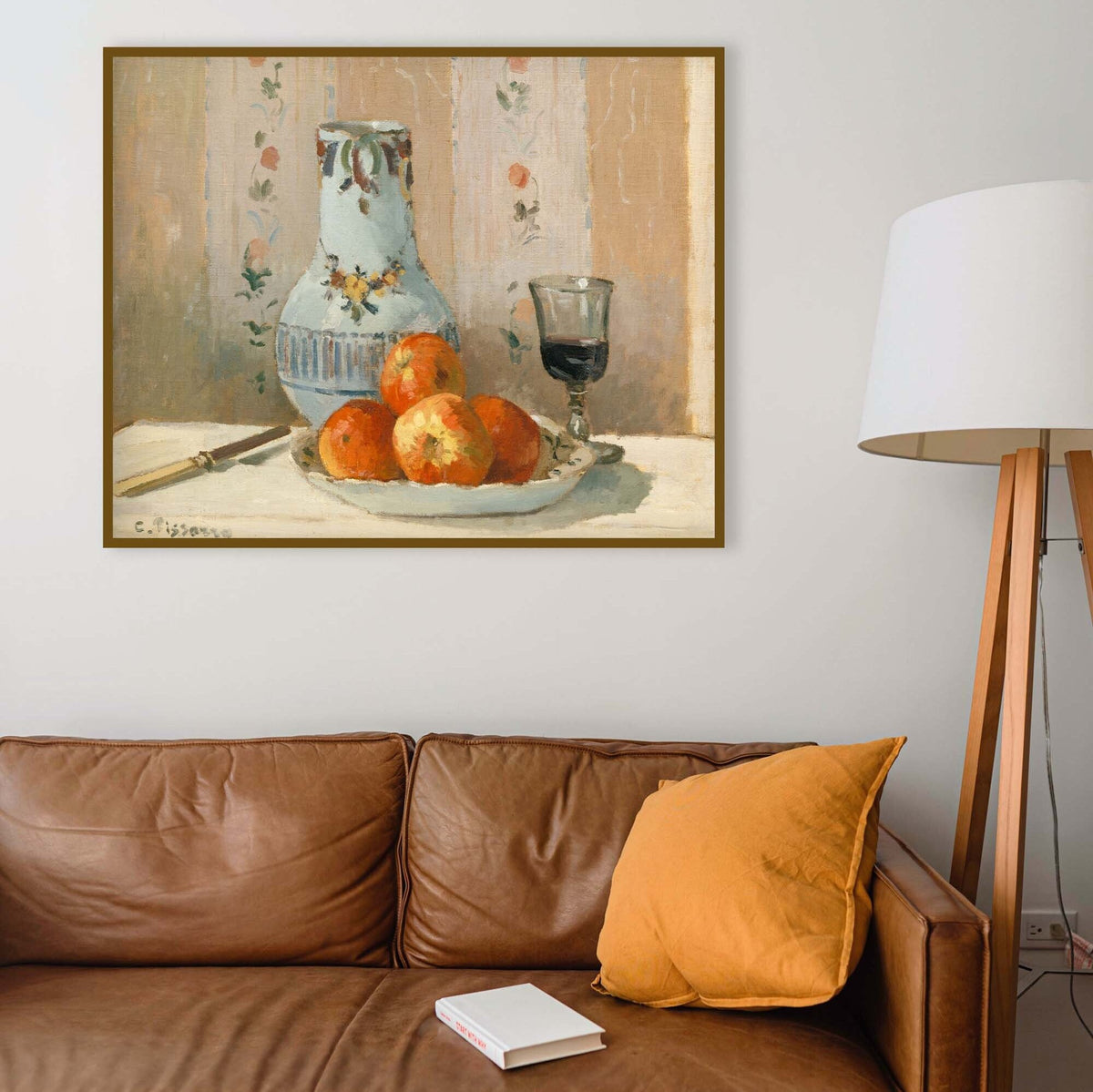 Framed painting of a still life with a vase and oranges above a brown leather sofa.