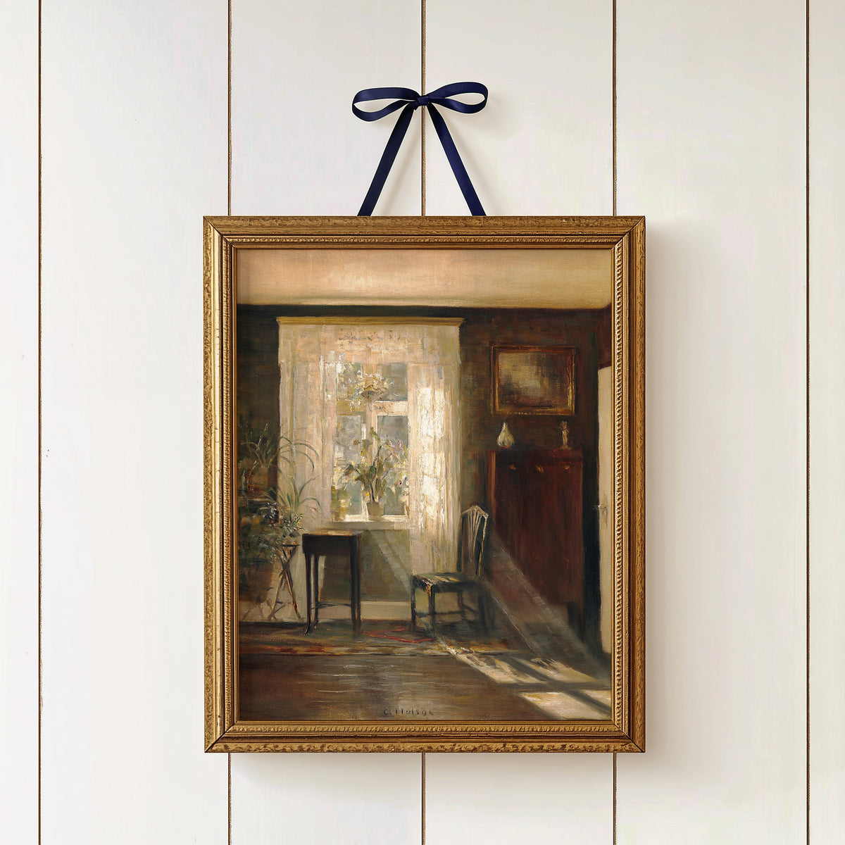 Framed print of an interior scene hanging in a gold frame with a blue ribbon on a white wall.